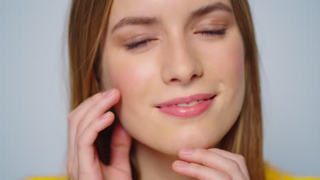 Closeup-attractive-smiling-woman-touching-face-with-hands-at-camera-indoors.