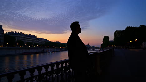 silhouette of a man on a bridge overlooking a city river at twilight