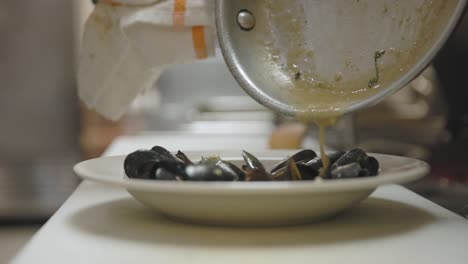 chef rociando salsa sobre mejillones en una cocina