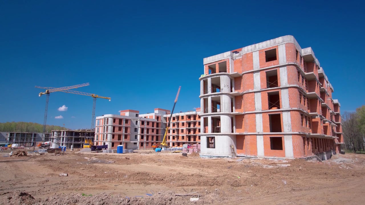 Grande cantiere edile con edifici in costruzione e case residenziali a più piani in timelapse. Gru a torre in azione su sfondo di cielo blu. Gru durante la casseratura.