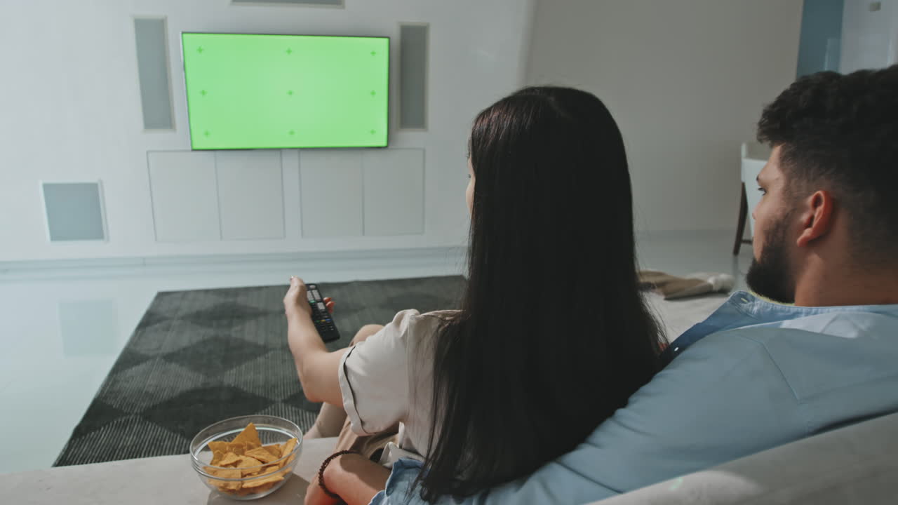 Giovane coppia guarda la TV e mangia nachos a casa