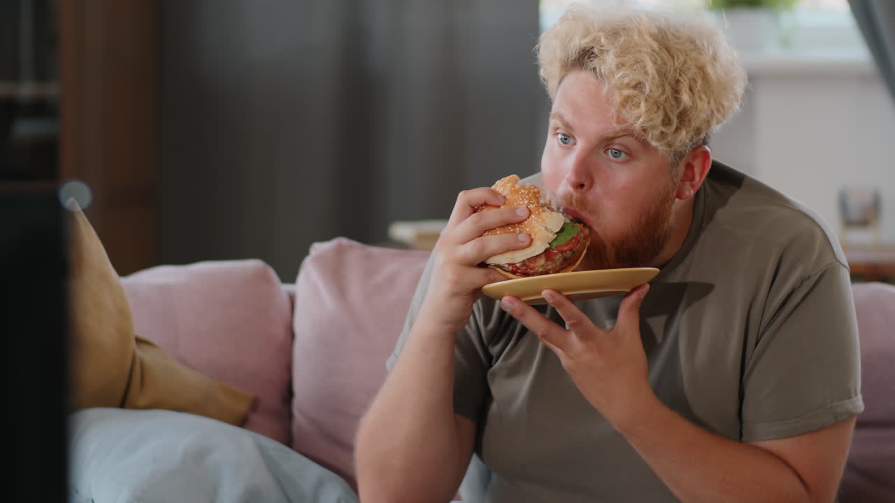 Obese Man Eating Burger and Watching TV at Home
