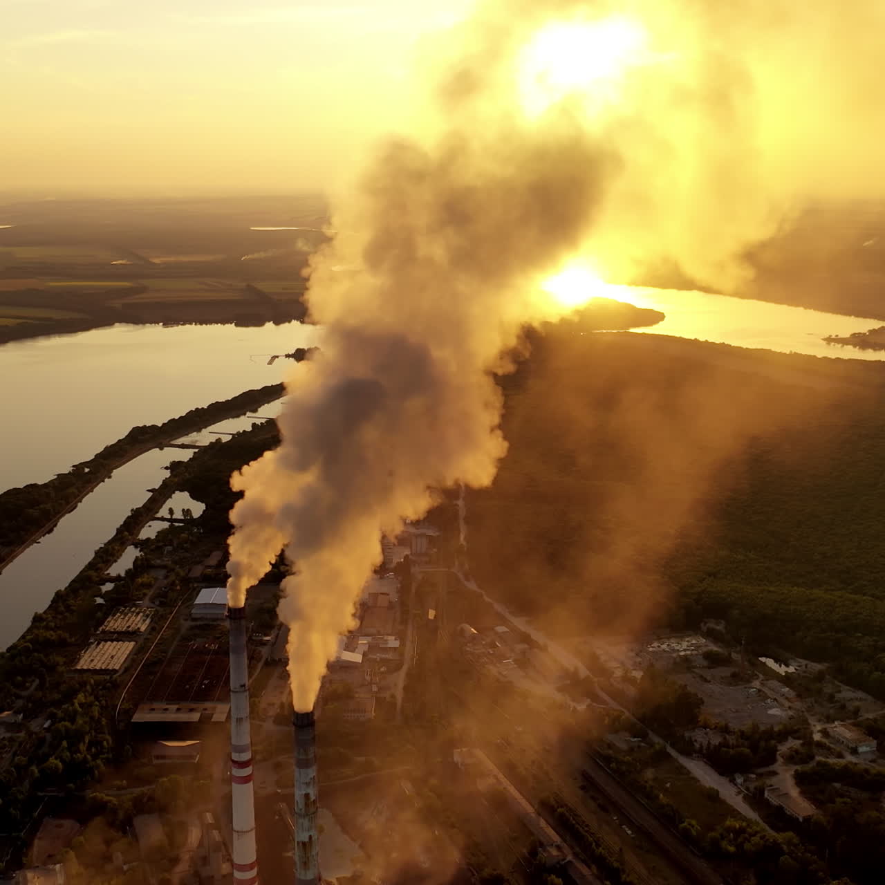 Power factory in nature at sunset. Thick smoke coming out from industrial pipes on the evening river background. Polluting the atmosphere. Aerial view.