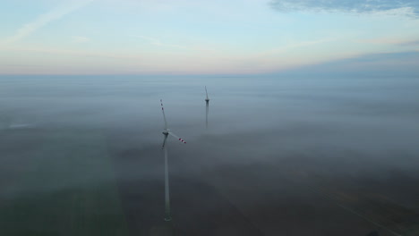 Aerial-view-of-wind-turbines-standing-on-agricultural-field-during-foggy-day