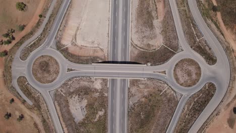 Aerial-view-looking-down-over-symmetrical-Portuguese-highway-roundabout-with-fast-cars-driving