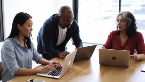 collaborative meeting among professionals engaged in discussion and problem-solving over laptops in a modern workspace setting