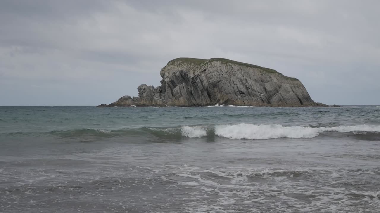 Rocky formation on Covachos Beach, Castro Island, with gentle waves and overcast skies