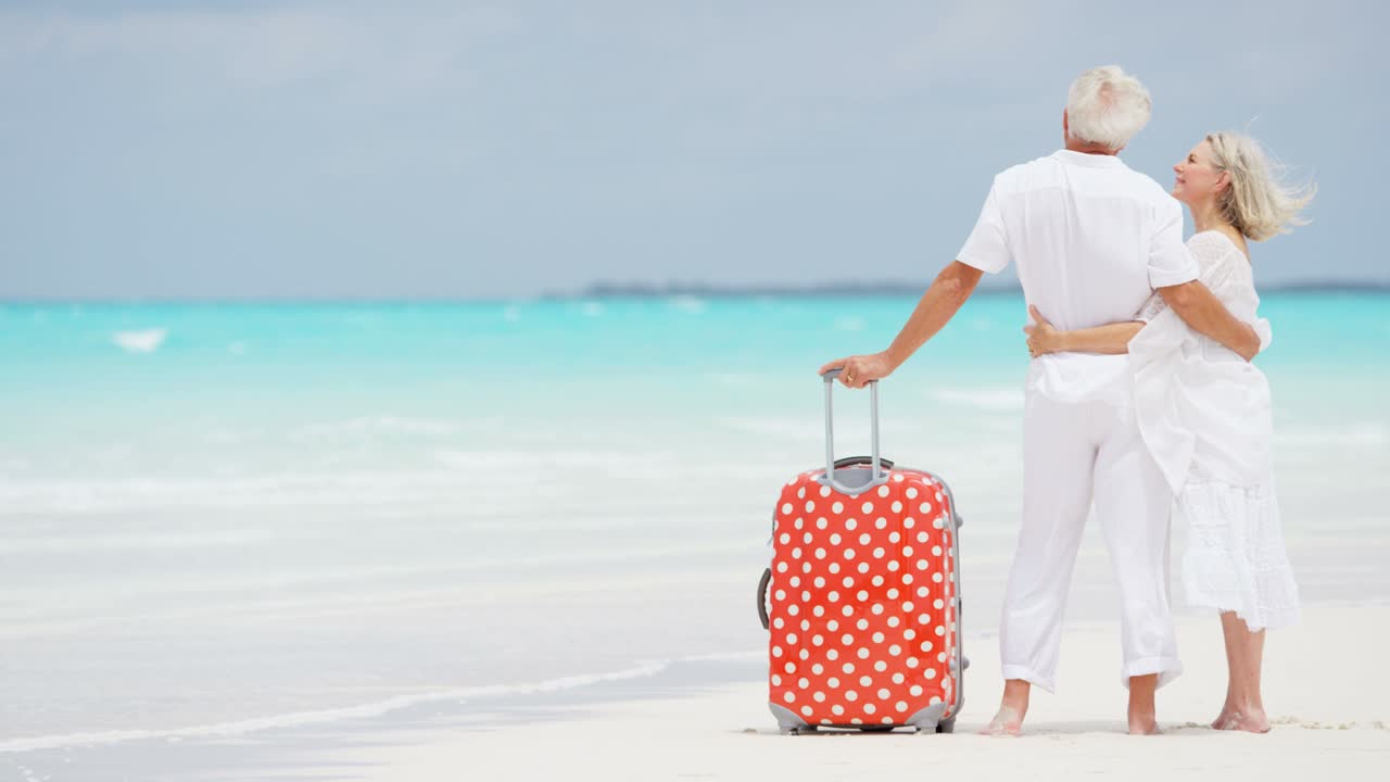 босоногая зрелая кавказская пара на пляже с чемоданом.