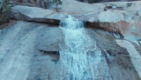 Pull-back-aerial-shot-of-cascading-water-fall-over-granite-rock