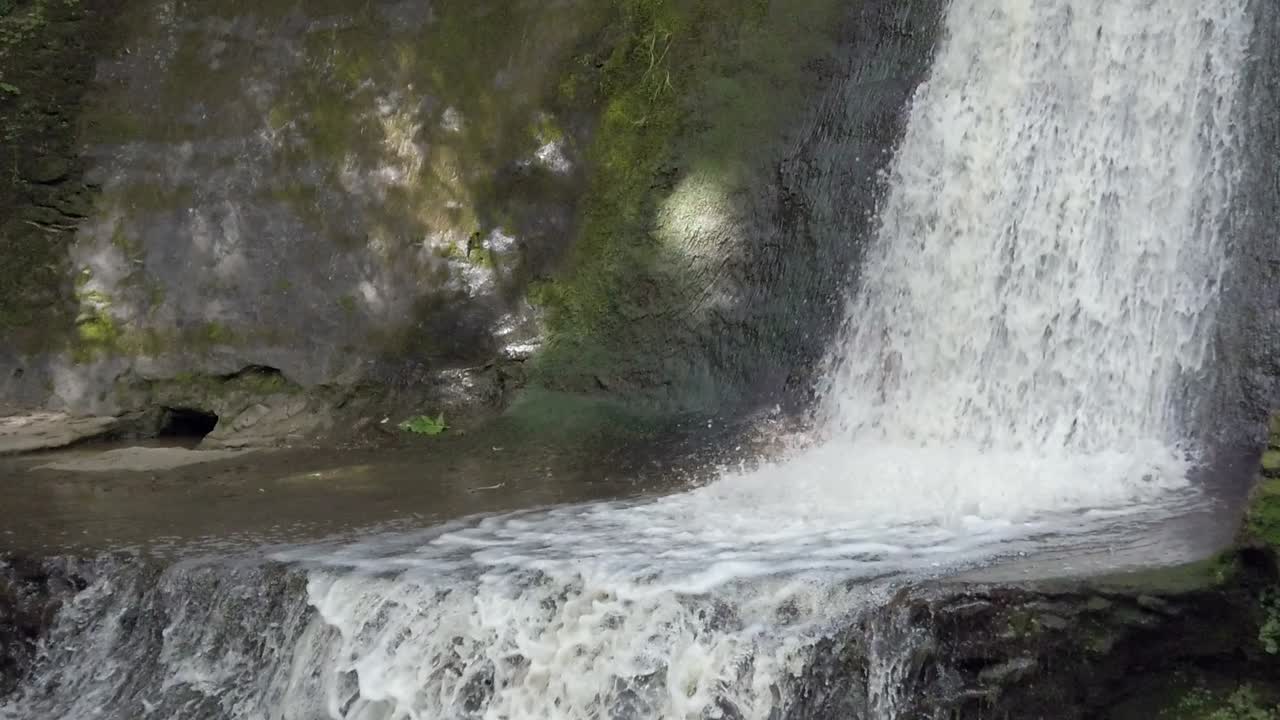 depósito de pared de piedra salpicando agua dulce a cámara lenta haciendo espuma en la base en el campo boscoso