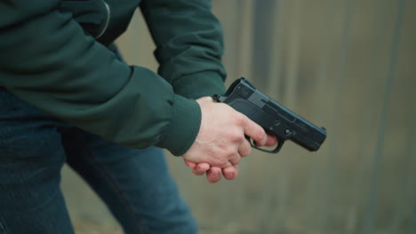 a close view of a man holding a black handgun with both hands, wearing a green jacket walking cautiously