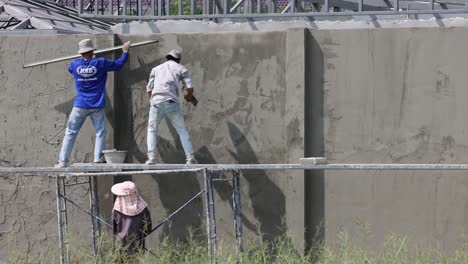 two workers applying plaster on an outdoor wall.