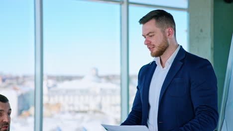 meeting on business indoors. handsome young businessman in blue suit talking to his partners about new blueprint on window background in the city.