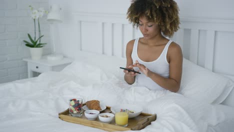 mujer encantadora usando el teléfono mientras desayuna