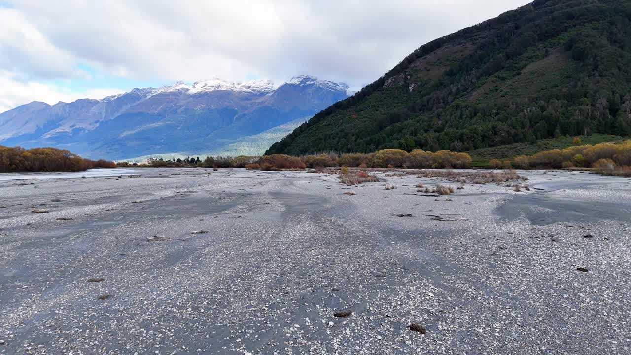 A tranquil riverbed with distant mountains under cloudy skies in Glenorchy, South Island. Captured with steady camera movement