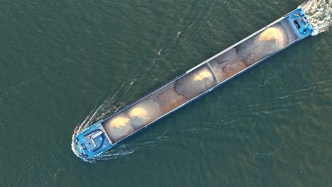 top-down following drone movement over the river drone dordrecht cargo ship with heavy ground cargo at mid oude maas distributary, zuid-holland, netherlands