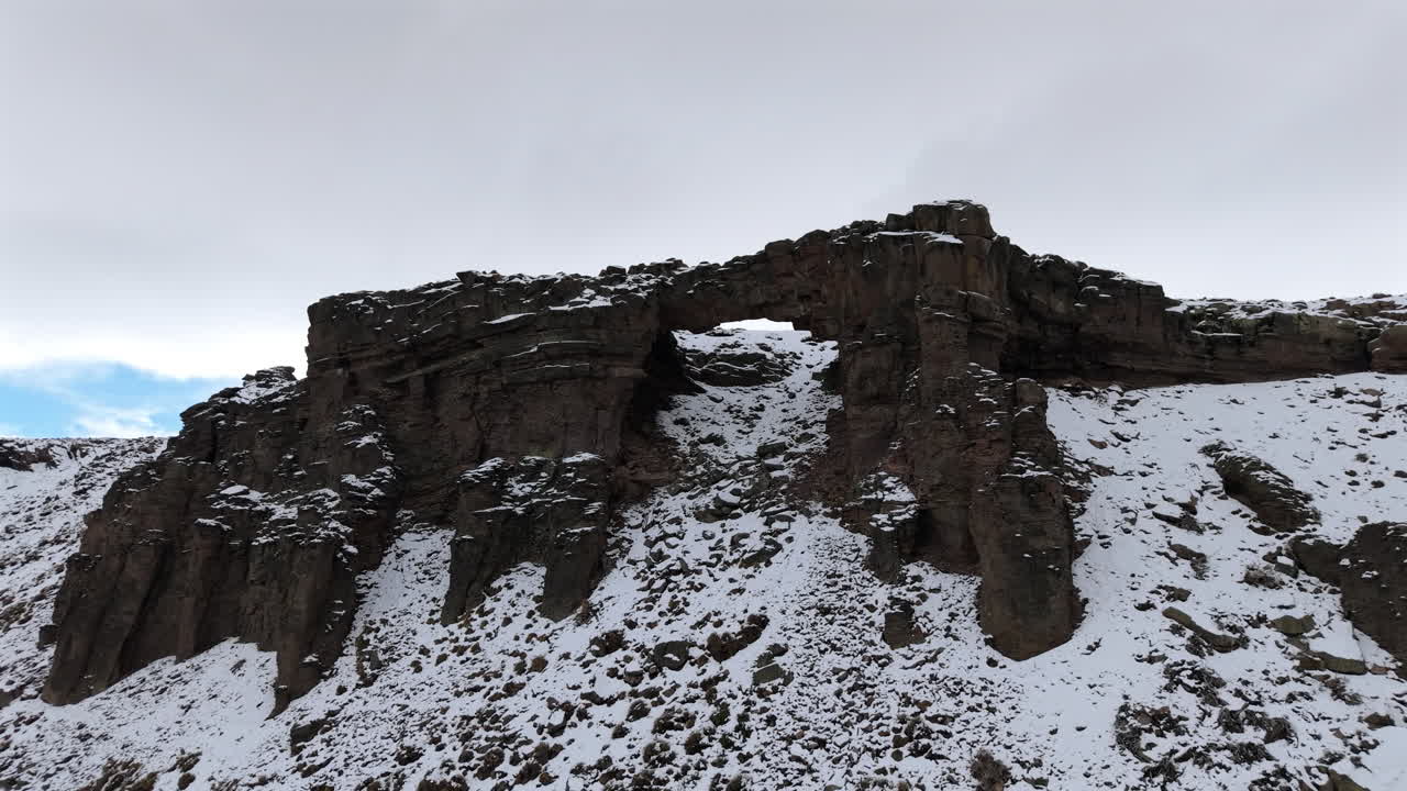 Foto de drone de uma enorme formação rochosa parcialmente coberta de neve sob um céu nublado de inverno na Patagônia, Argentina
