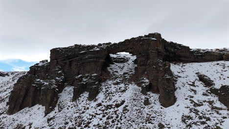 Drone shot of a massive rocky formation partially covered in snow under a cloudy winter sky in Patagonia, Argentina
