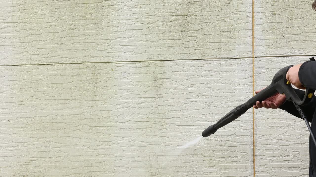 Uomo che pulisce le pareti con un'idropulitrice ad alta pressione. Lavaggio delle pareti esterne di una casa