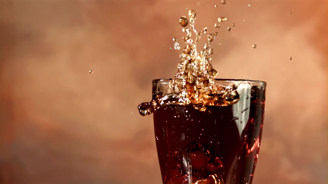 Cubito de hielo cayendo en cámara lenta en un vaso de cola refrescante