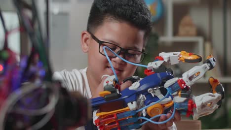 close up of satisfied asian cute boy looking and checking a cyborg hand while working on a laptop at home