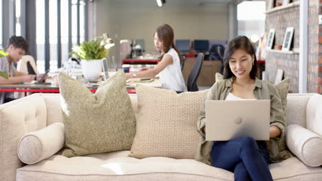 working on laptop, woman sitting on couch in modern office space