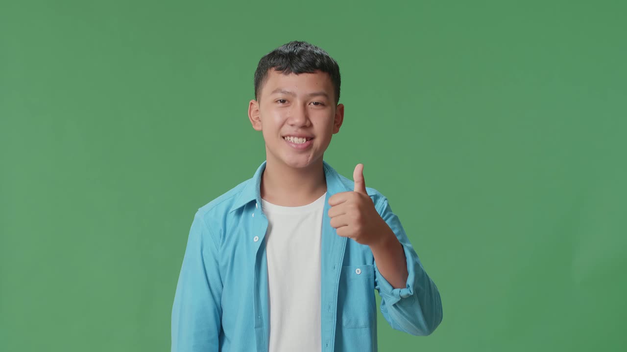 Happy Young Asian Boy Showing Thumbs Up Gesture While Standing In The Green Screen Studio