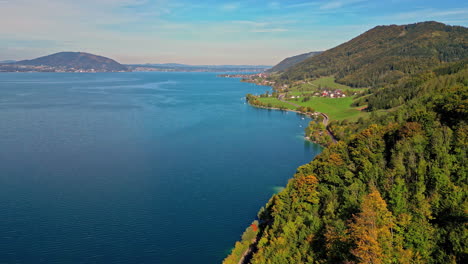 aerial panning shot of attersee in austria, showcasing autumn foliage and clear blue waters