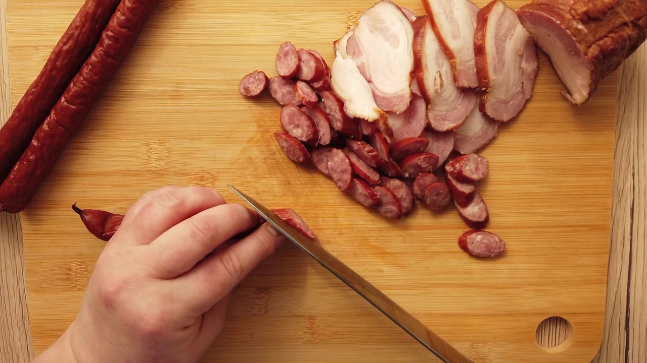 Il cuoco taglia salsiccia affumicata con pancetta su un tagliere