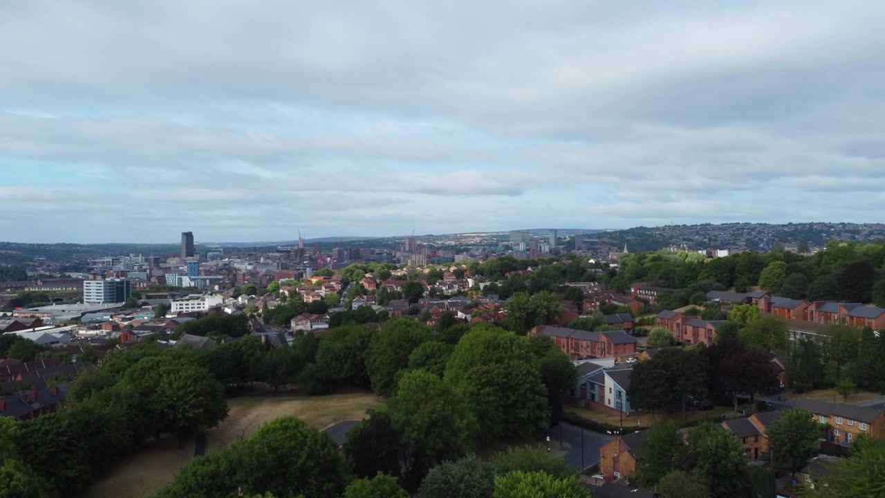 Rekaman drone udara yang naik di atas pepohonan menampakkan cakrawala kota Sheffield pada hari yang cerah dengan awan yang tersebar. Pengambilan gambar pembuka sinematik yang menghadap Yorkshire Selatan, Inggris.