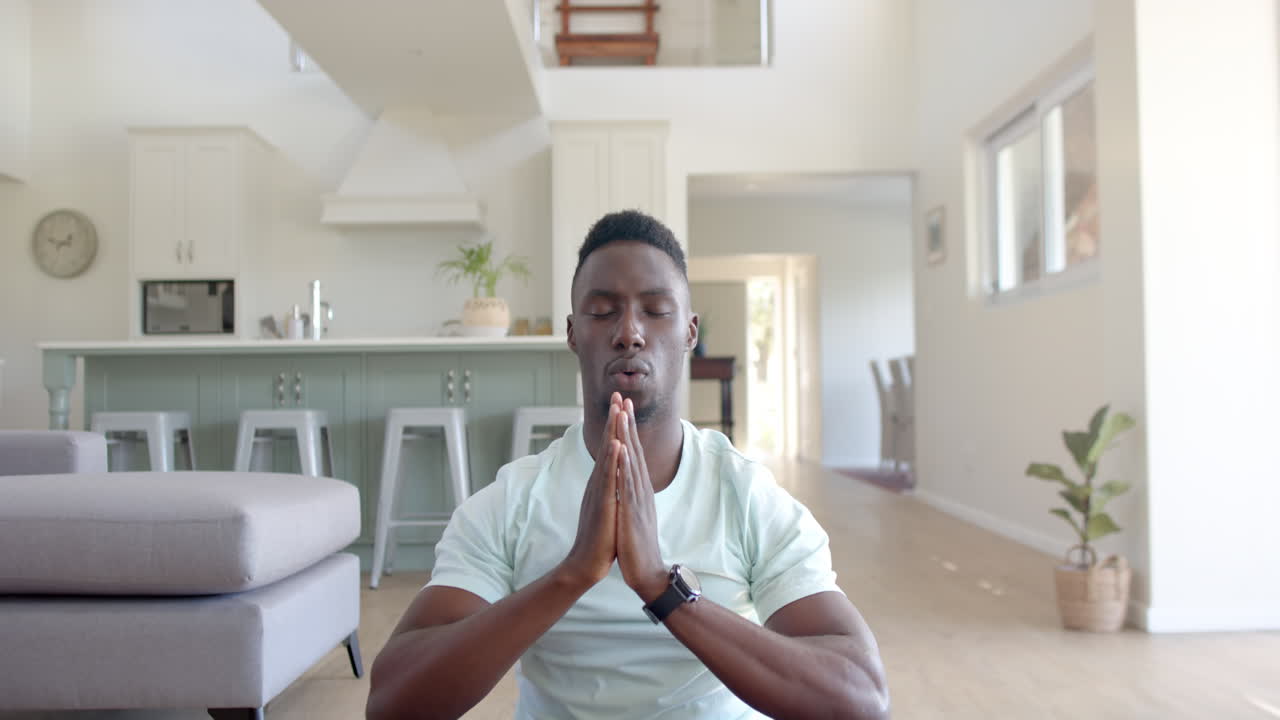 Focused african american man practising yoga meditation in sunny living room, slow motion