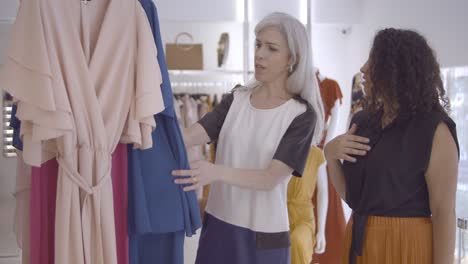 positive female friends choosing clothes in fashion store