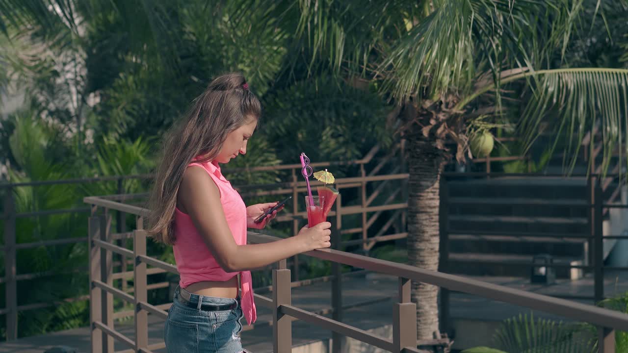 una dama con blusa rosa y pantalones cortos de vaqueros está en el patio del hotel.