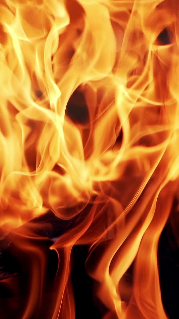 Detailed motion of orange flame on the black background. Close-up bright fantastic flame on firewoods outdoors. Vertical video