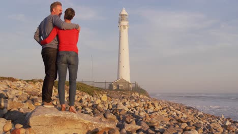 couple embracing by the sea near a lighthouse