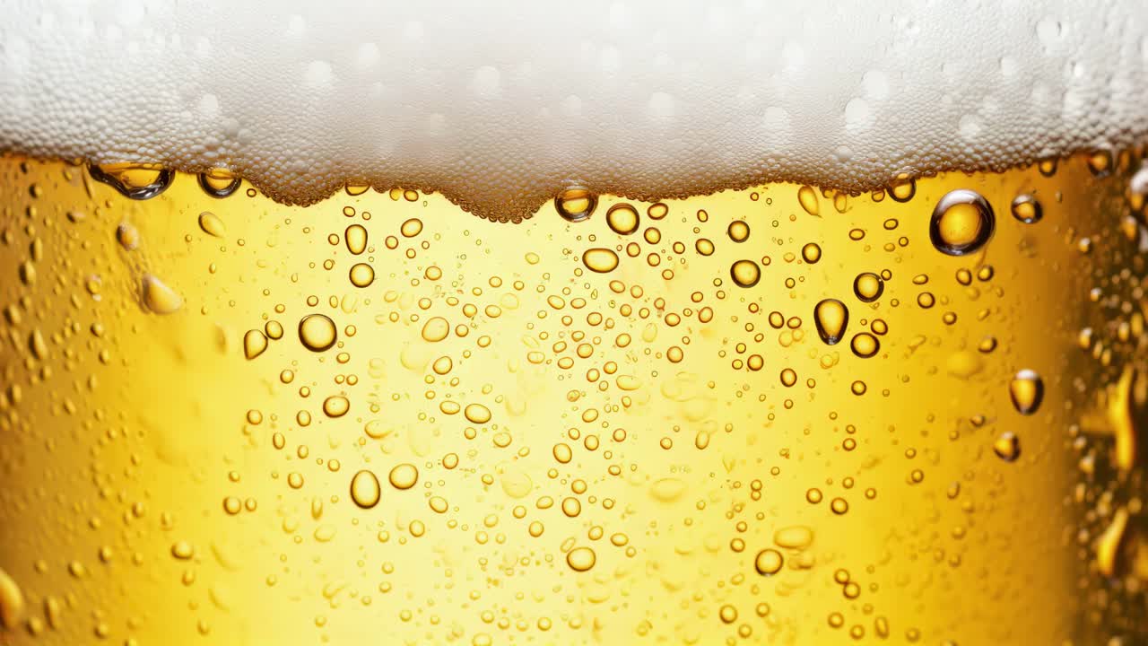 泡立ったビールの表面と気泡のクローズアップ映像スチル。ローアングルから撮影されています。