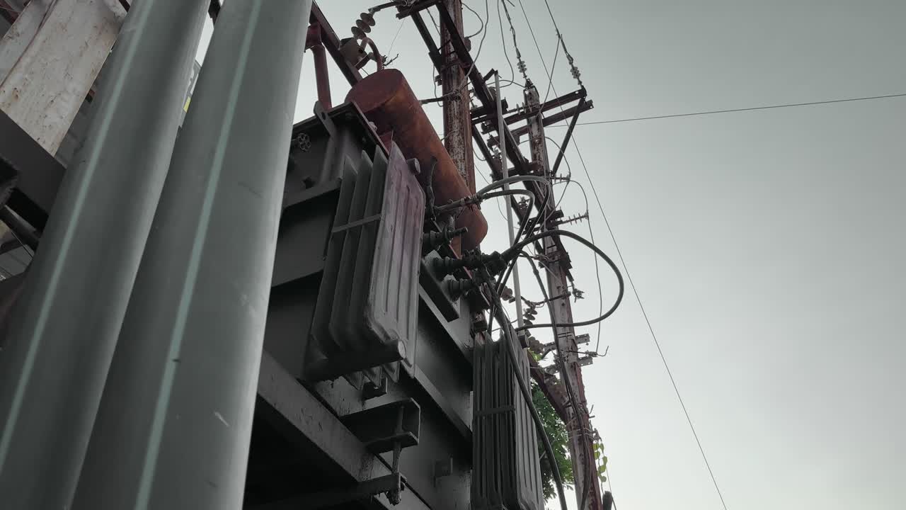 A camera slowly rotates around an old transformer with exposed and tangled electrical wires connected to utility poles. highlighting decaying infrastructure and unsafe wiring