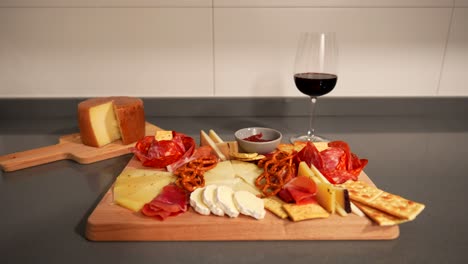 manos femeninas tomando un vaso de vino rojo al lado de una tabla de queso con pan y pretzels