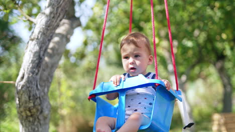 sweet barefoot baby sits on a swing. little kid having fun outdoors in the garden on warm sunny day. blurred backdrop.