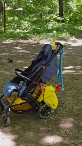 baby boy wearing bright yellow blazer sits near his stroller looking for something. kid stands up runs away and throws something ahead. vertical video.
