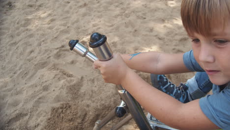 a child shovels sand using toy metal excavator on the playground during summer