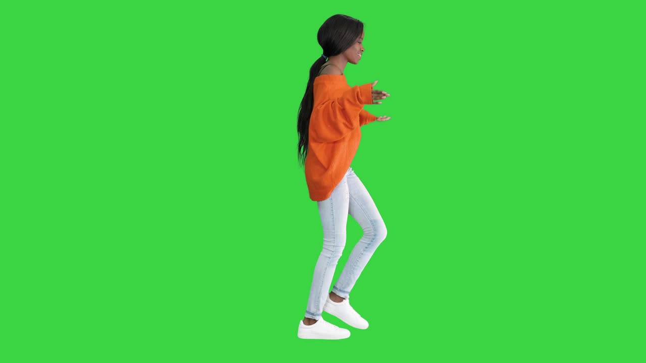 밝은 캐주얼 옷을 입은 편안한 아프리카계 미국인 젊은 여성이 녹색 스크린, 크로마 키에서 는 동안 춤을 추고 있습니다.