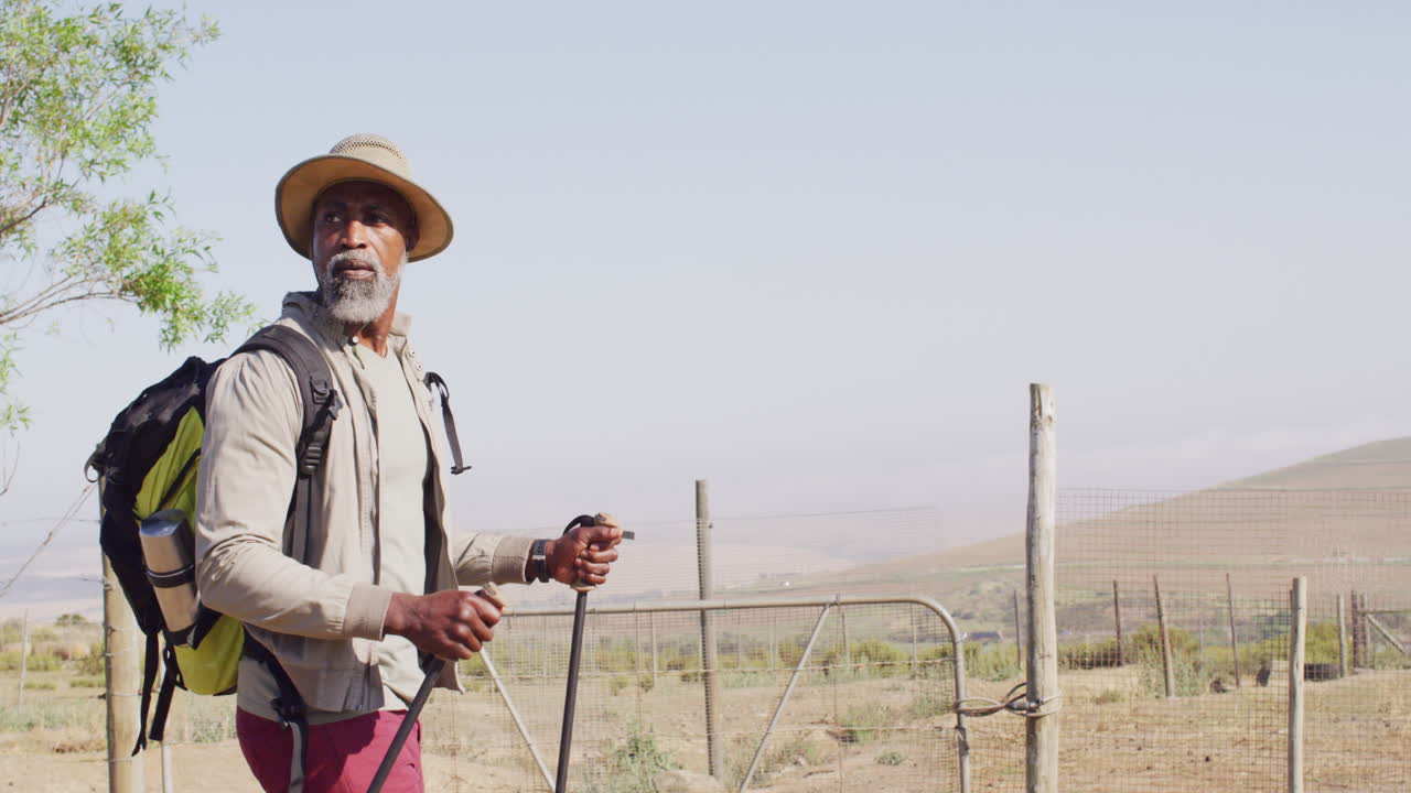 Senior african american man hiking with trekking poles on sunny day, slow motion