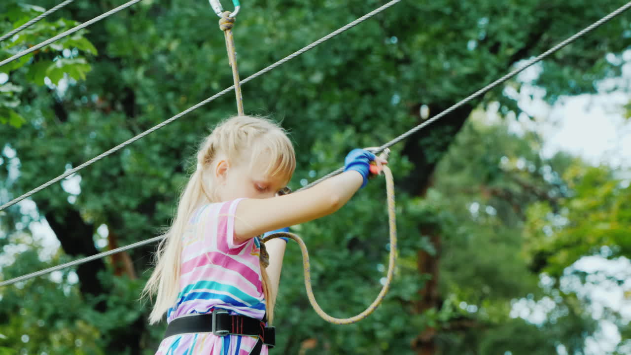 la vista trasera de una chica valiente se mueve a lo largo de las cuerdas entre los árboles usa una cuerda de seguridad