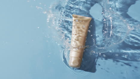 video de un tubo de producto de belleza en el agua con espacio de copia en fondo azul