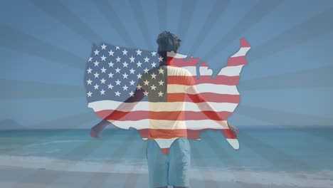 Animation-Einer-Karte-Mit-Amerikanischer-Flagge,-Die-über-Einem-Mann-Mit-Ausgestreckten-Armen-Am-Strand-Winkt