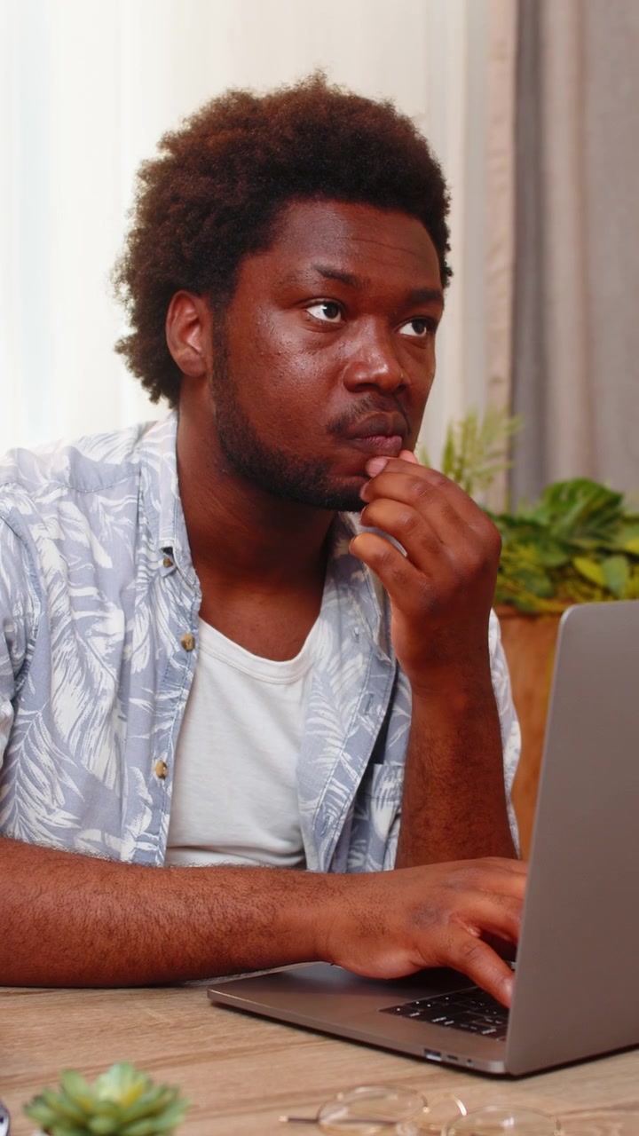 African american young man on home table checks email on laptop thinks then starts writing a reply