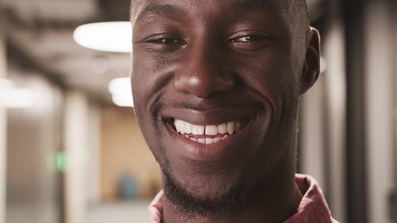 Uomo afroamericano sorridente nel corridoio di un ufficio, che esprime felicità e positività al lavoro.