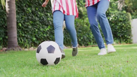 Video-of-low-section-of-biracial-mother-and-daughter-playing-soccer-in-garden