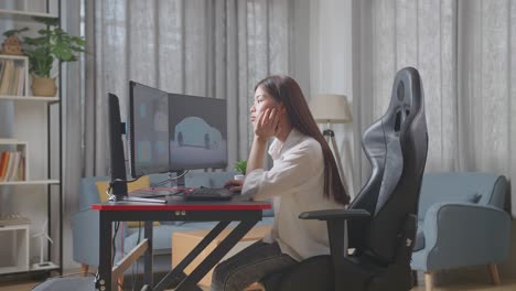 side view of asian female automotive designer holding hands on cheek while working boringly on 3d model of ev car on the desktop computers in the studio